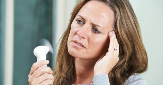 Woman using a hand held fan to cool a hot flush