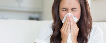 Close up of woman with a cold blowing her nose with a tissue.