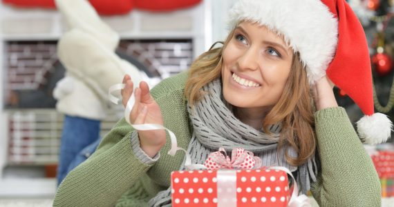 Happy woman wearing Christmas hat, relaxing on the floor with a present