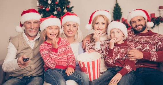 Multi-generational family wearing Christmas hats sitting on a sofa smiling