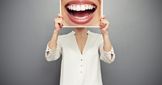 Woman holding an oversized photo of a smiling mouth over her face