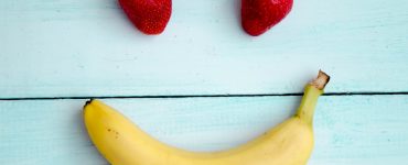 two strawberries and a banana made to look like a happy face on a blue wooden background